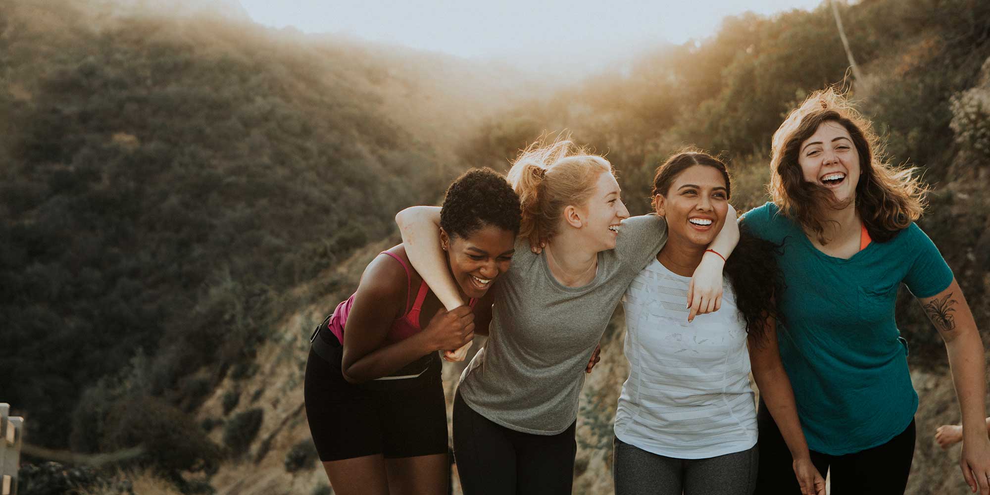 Four women embrace laughing on a sunset hike